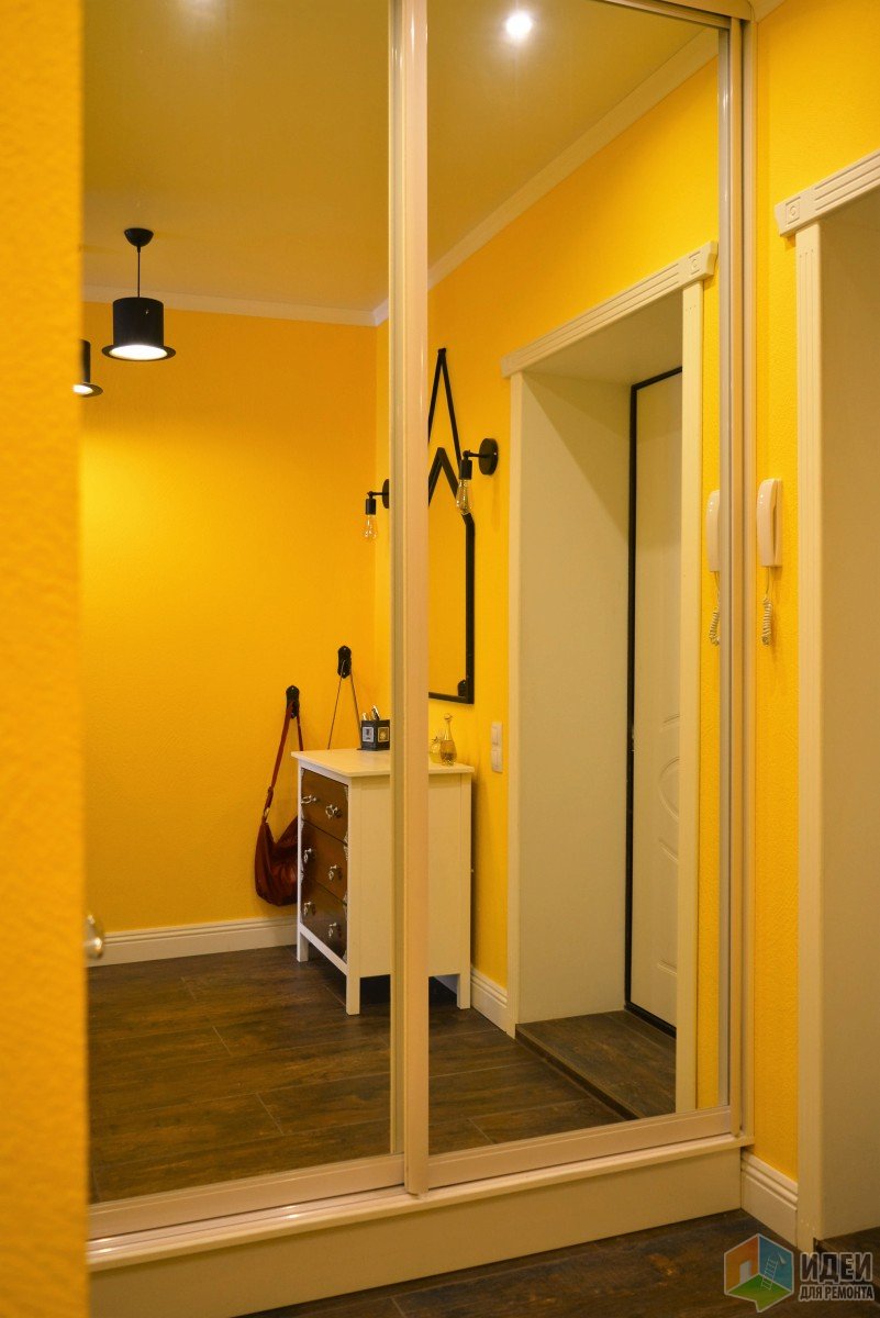 Маленькая желтая прихожая с зеркальным шкафом-купе, тумбой и оригинальными лампами Эдиссона
