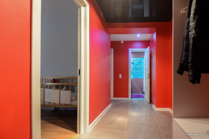 Длинный Г-образный коридор с красными стенами, натяжным потолком и плиткой на полу